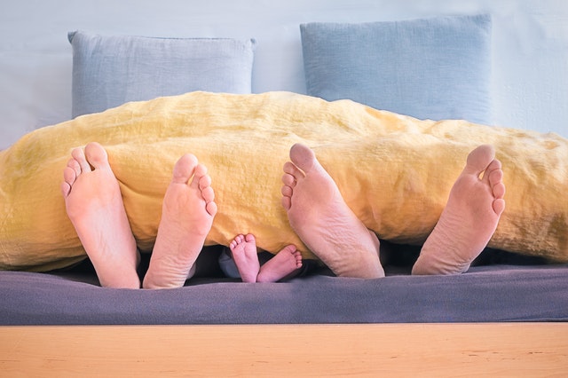 Family of Three Lying on Bed Showing Feet While Covered With Yellow Blanket